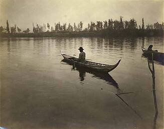 Tanana man in canoe next to fish net, Tanana River, Alaska, 1914.